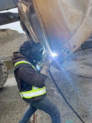 Welder in full protective gear working on a loader bucket on site